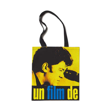 A yellow and black tote bag featuring a graphic print of a person's profile and the text 'un film de' in blue. Pedro Almodovar director tote bag